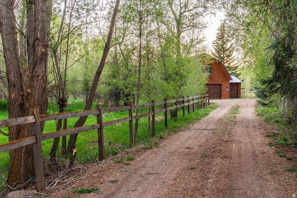 Gravel driveway bordered by a split-rail fence and mature trees