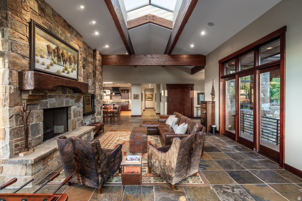 Spacious living area featuring a floor-to-ceiling stone fireplace with a substantial wood mantel, skylights, exposed wood beams, and large glass panel doors
