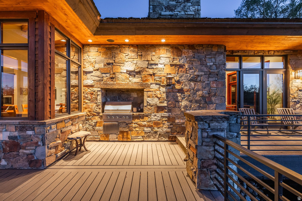 Expansive outdoor deck featuring wood-finish flooring, stone-clad exterior walls, built-in grill, and contemporary railings