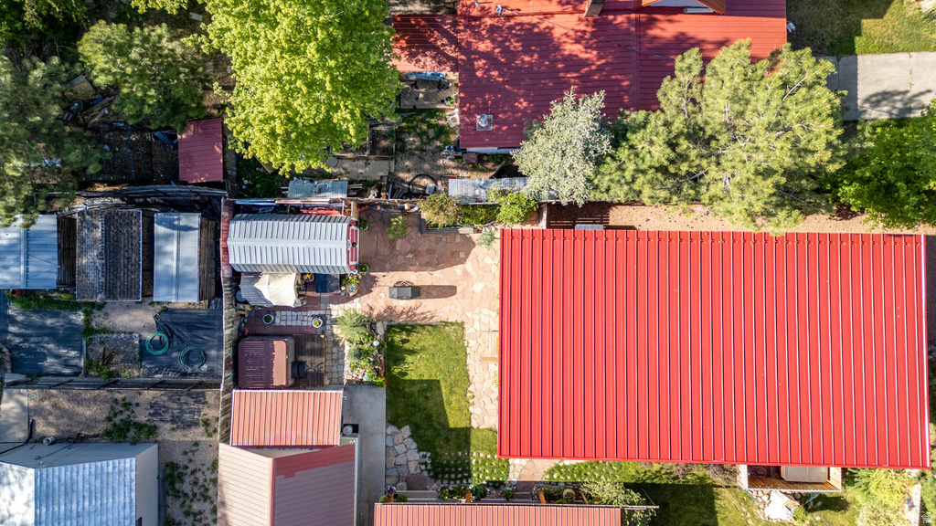 Aerial property view featuring a red metal roof, mature trees, a stone patio, and a manicured lawn