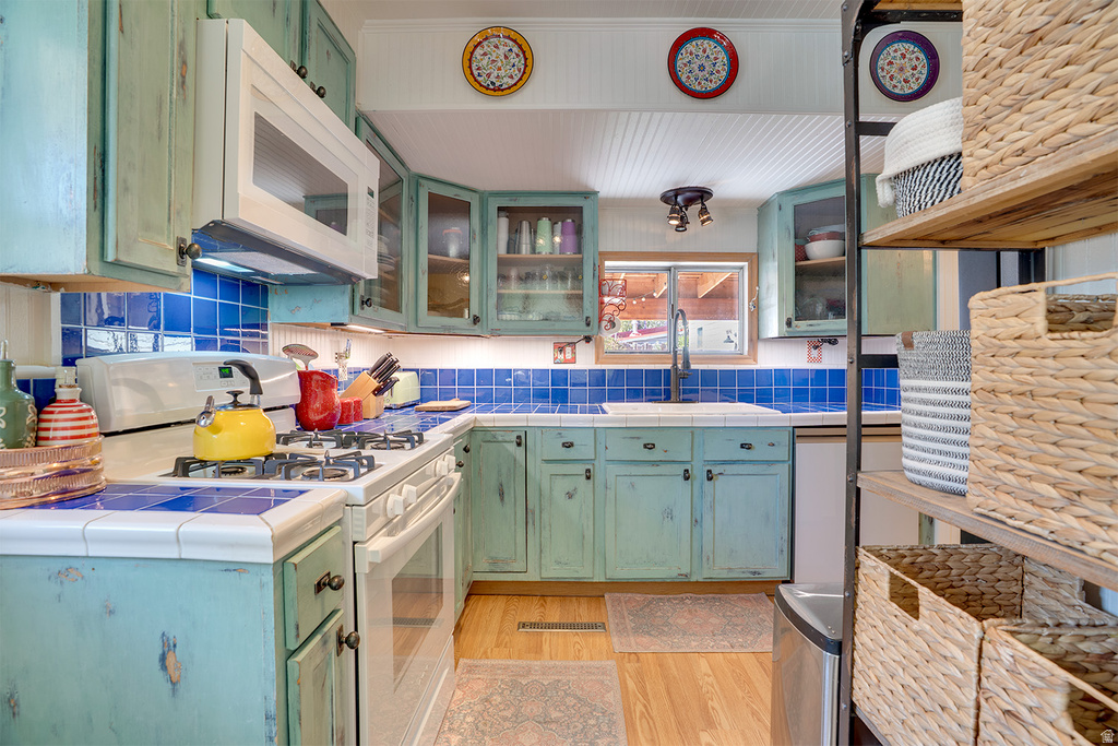 Kitchen featuring distressed teal cabinetry, blue tile countertops, and a matching tile backsplash