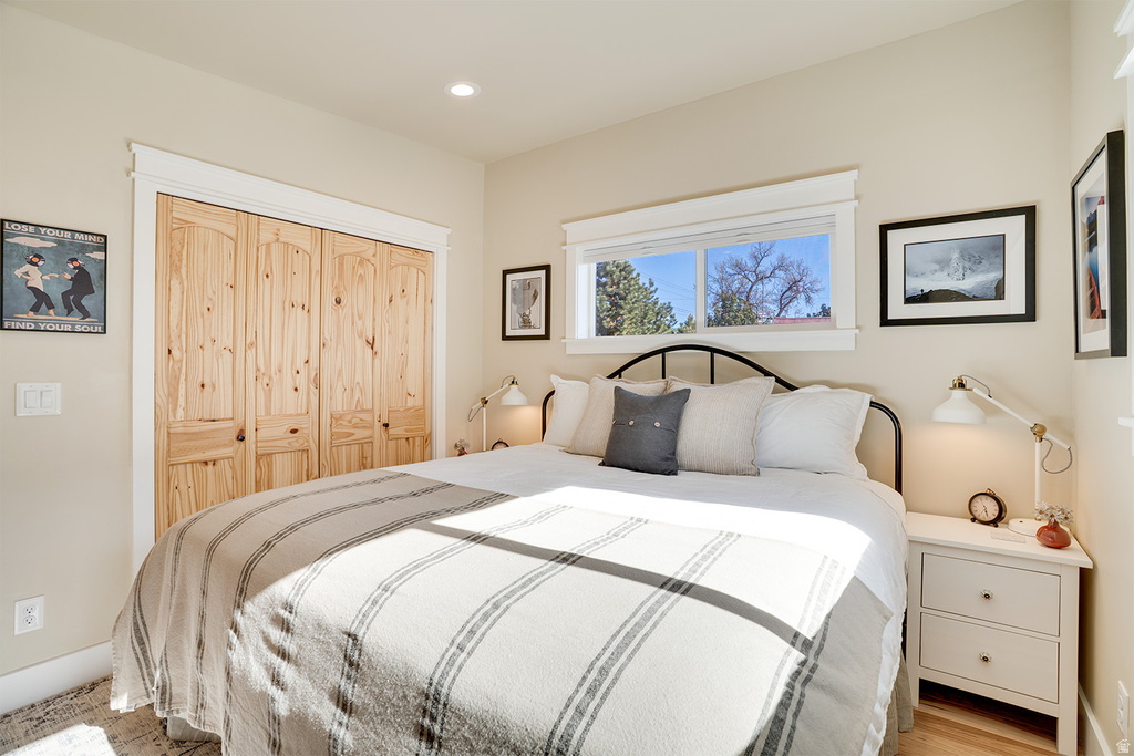 Bedroom featuring a large window, light wood-finish flooring, recessed lighting, and natural wood bi-fold closet doors with arch top panels