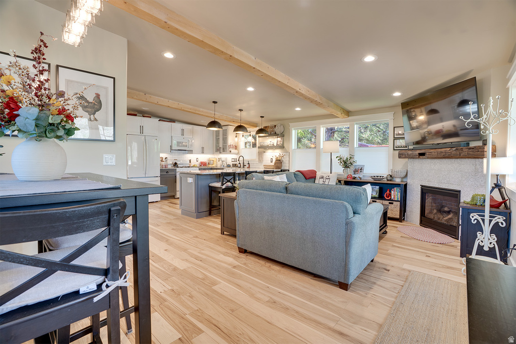 Open-concept living space featuring wood-finish flooring, exposed ceiling beams, recessed lighting, a stone-surround fireplace with wood mantel, and a kitchen with an island and pendant lighting