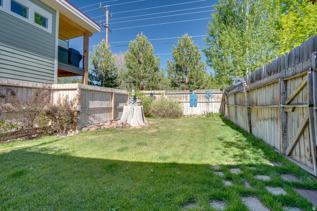 Expansive grassy yard featuring a private wood fence perimeter, mature landscaping, and square stepping stones