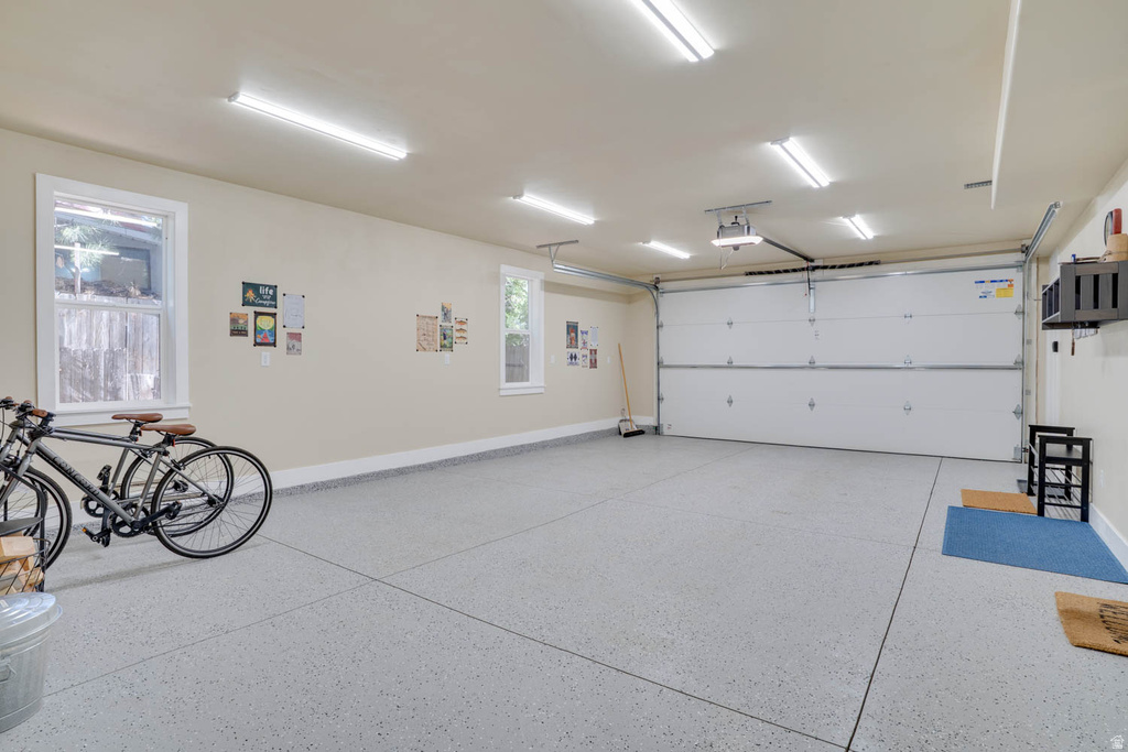 Spacious garage featuring a light gray speckled epoxy floor, multiple windows, ample overhead lighting, an automatic garage door, and light-toned wall paint