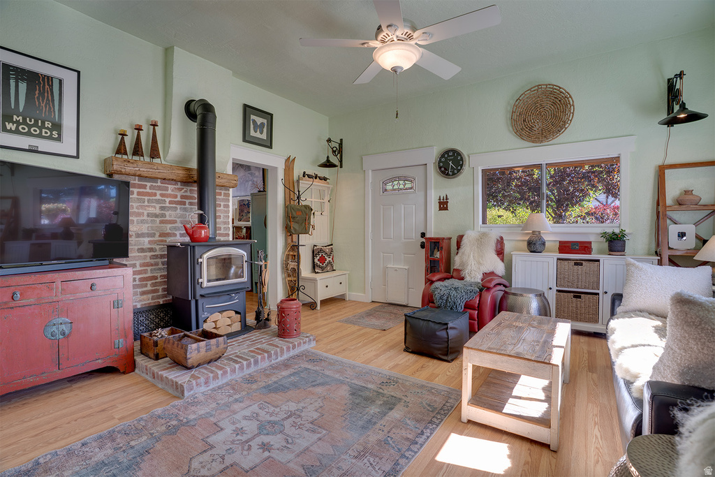 Living area featuring wood-finish flooring, a brick-surround wood stove with a timber mantel, a ceiling fan, and painted trim