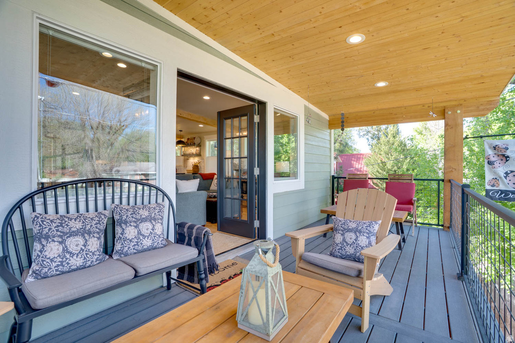 Covered outdoor deck featuring composite decking, wood plank ceiling, recessed lighting, and a black metal railing