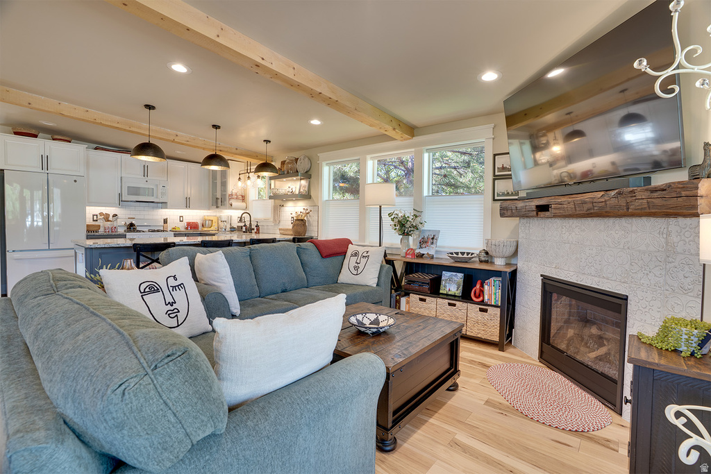Living area with wood-finish flooring, exposed ceiling beams, and a tiled fireplace featuring a substantial wood mantel