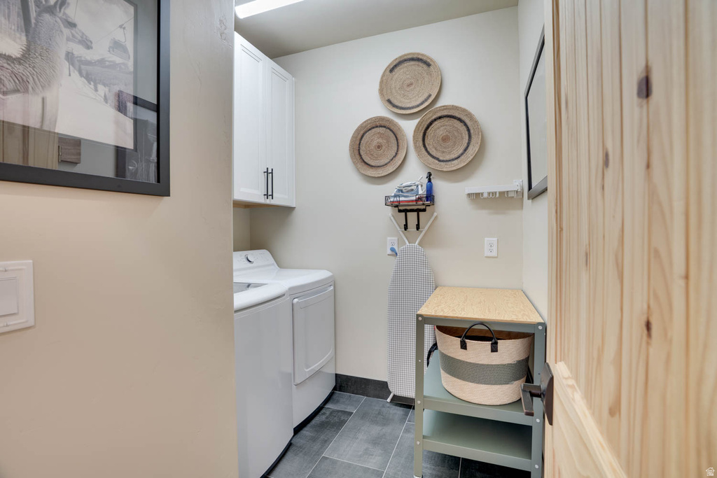Laundry area featuring white cabinetry with dark pulls, a light wood-finish door, and dark tile flooring