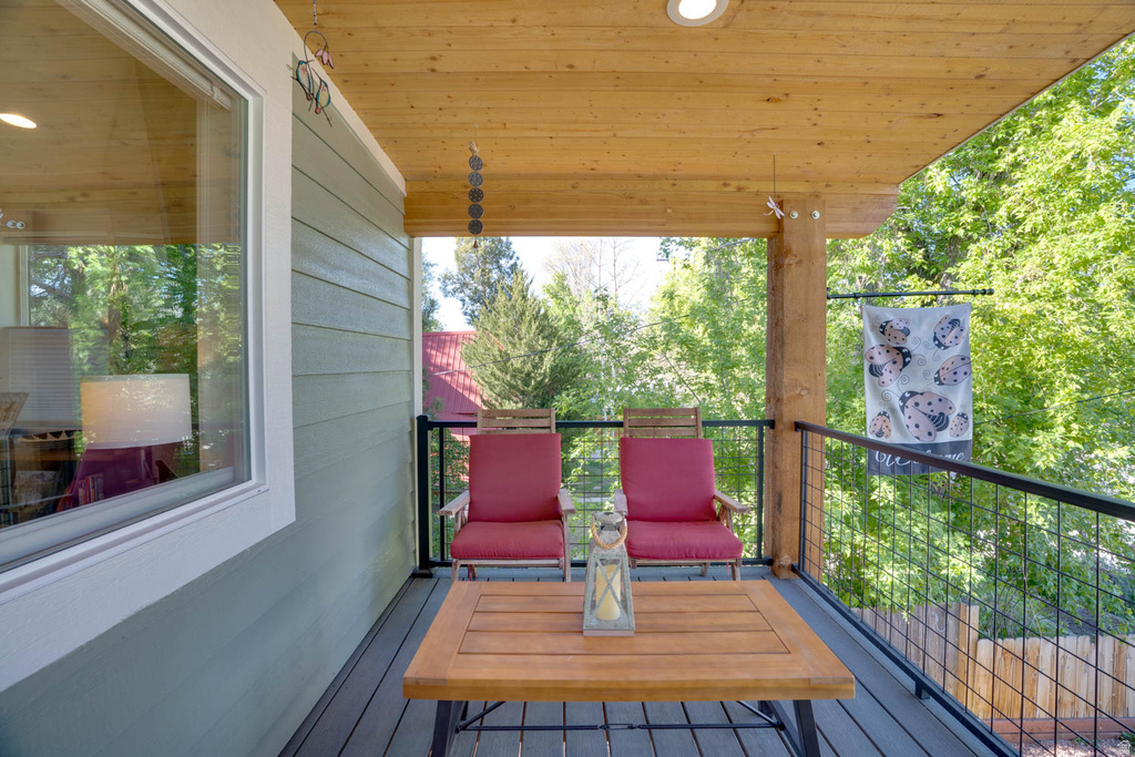 Covered outdoor deck featuring composite decking, wood-finish ceiling, recessed lighting, and a black metal railing