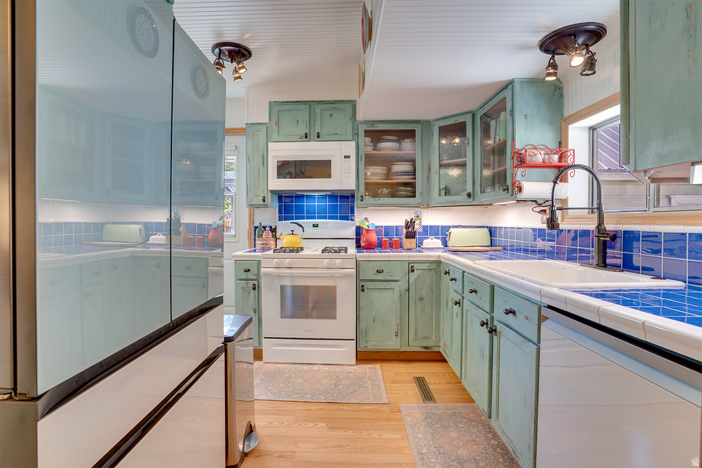 Kitchen featuring distressed green cabinetry, blue square tile backsplash, and light wood-finish flooring