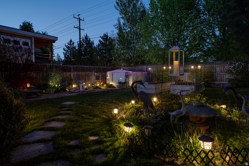 Landscaped backyard featuring a stone-stepped path, mature shrubbery, a wood privacy fence, a detached shed, and multiple integrated outdoor lighting fixtures