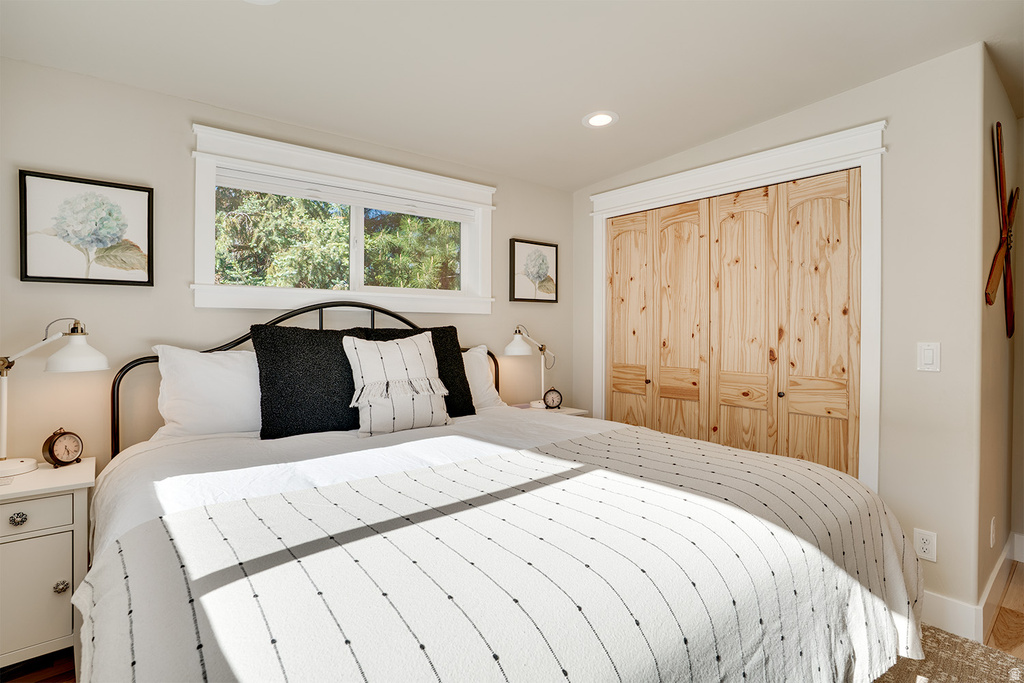 Bedroom featuring a wide window with white trim, recessed lighting, and a closet with natural wood bi-fold doors