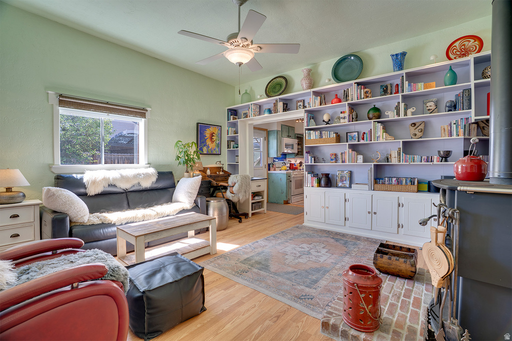Living area featuring wood-finish flooring, a ceiling fan with light fixture, and a window with blinds