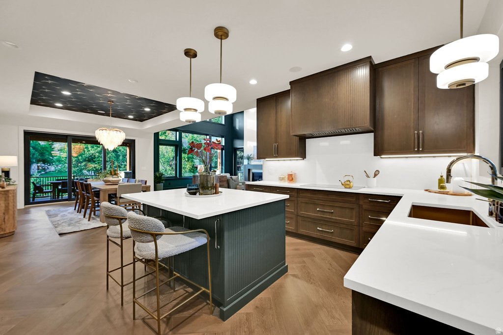 Open-concept kitchen featuring an island with seating, dark wood-finish cabinetry, white countertops, herringbone wood-finish flooring, and pendant lighting