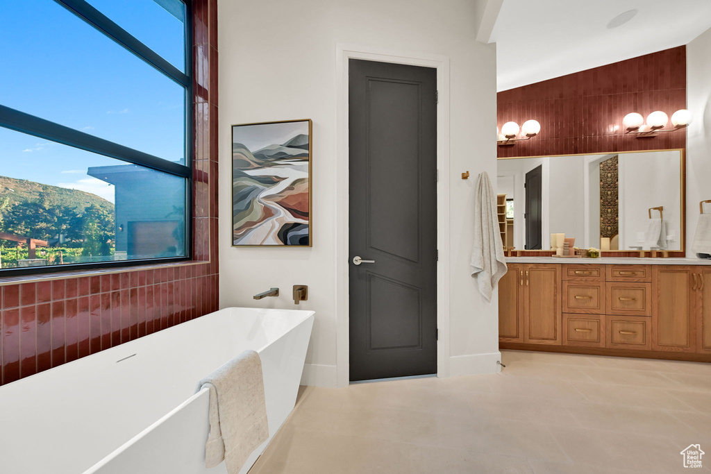 Contemporary bathroom featuring a freestanding tub, large window, wood-finish vanity with dual sinks, and a textured accent wall with wall-mounted sconces