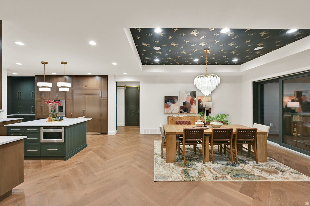 Open-concept living space featuring wood-finish flooring in a herringbone pattern, a kitchen island with integrated microwave, built-in cabinetry, recessed lighting, and a tray ceiling with decorative wallpaper and a central chandelier
