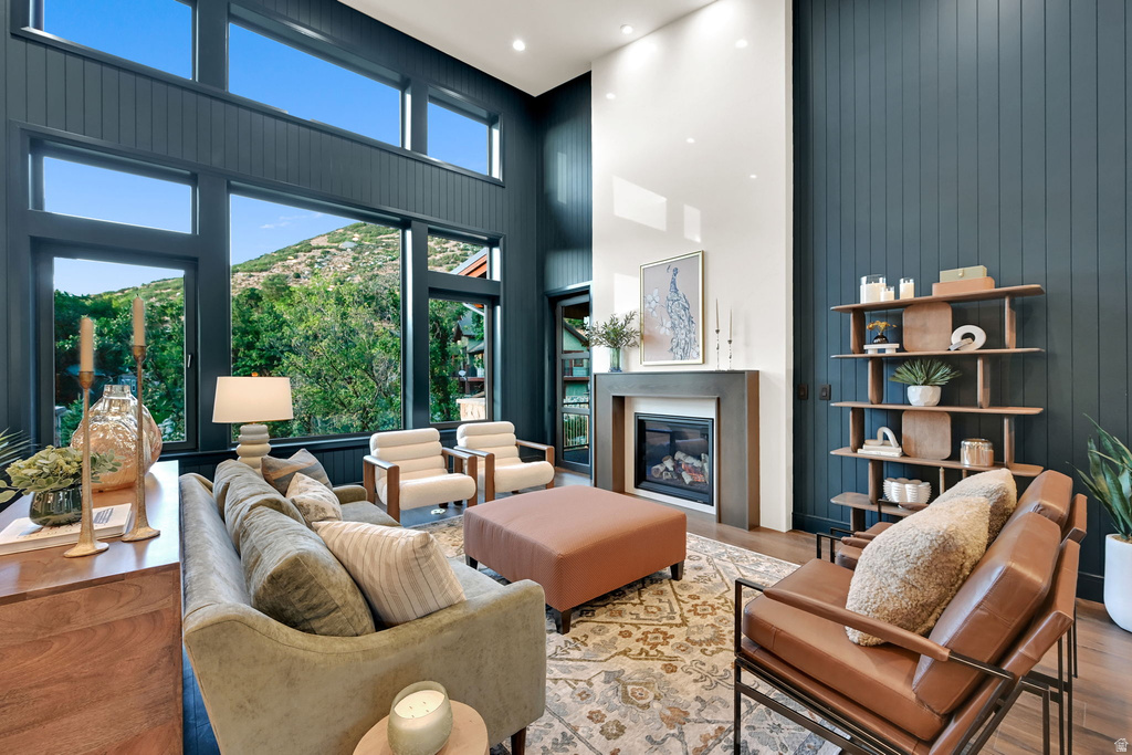 Living room featuring a tall ceiling, extensive windows, a gas fireplace with a surround, a built-in shelving unit, and wood-finish flooring