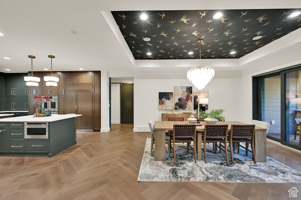 Open-concept living space featuring herringbone wood-finish flooring, a kitchen island with built-in microwave and white countertop, dark wood cabinetry, a recessed ceiling with a decorative pattern, and a sliding glass door