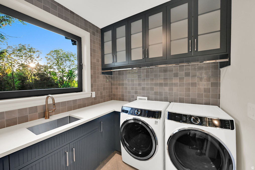 Utility room featuring a large window, square tile backsplash, white countertops, and dark shaker-style cabinetry with glass inserts