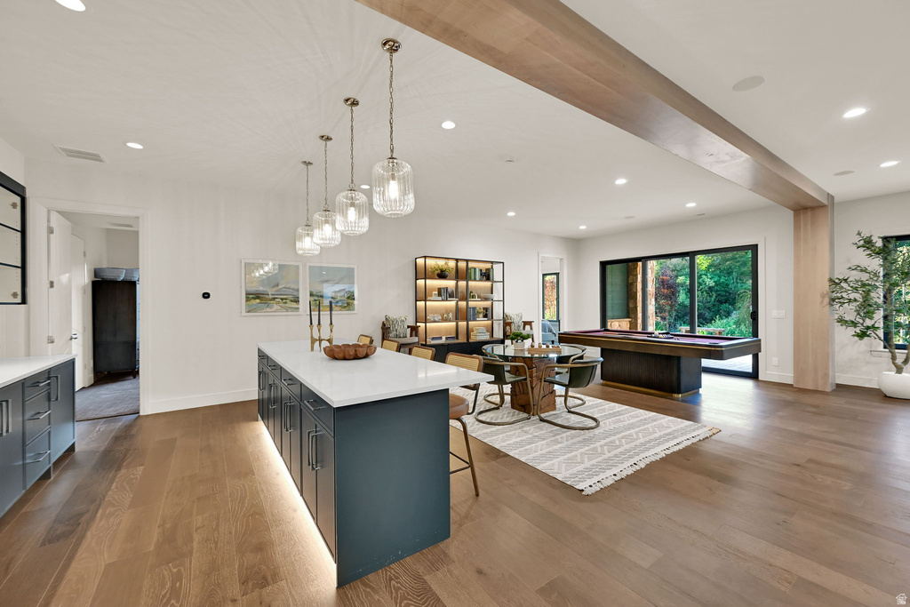 Open-concept entertainment space featuring wood-finish flooring, a kitchen island with pendant lighting, built-in shelving, and large sliding glass doors