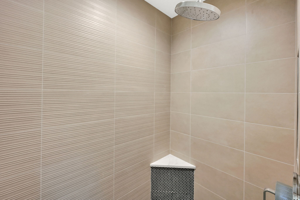 Shower enclosure featuring a rain shower head, textured wall tiling, smooth wall tiling, and a corner shelf with mosaic tile accents
