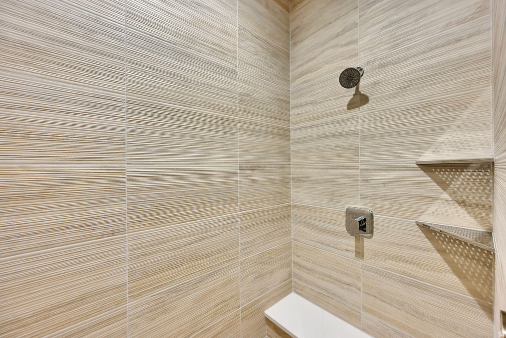 Shower enclosure featuring large format stone-finish tile, a rainfall showerhead, polished chrome controls, an integrated bench, and two built-in corner shelves
