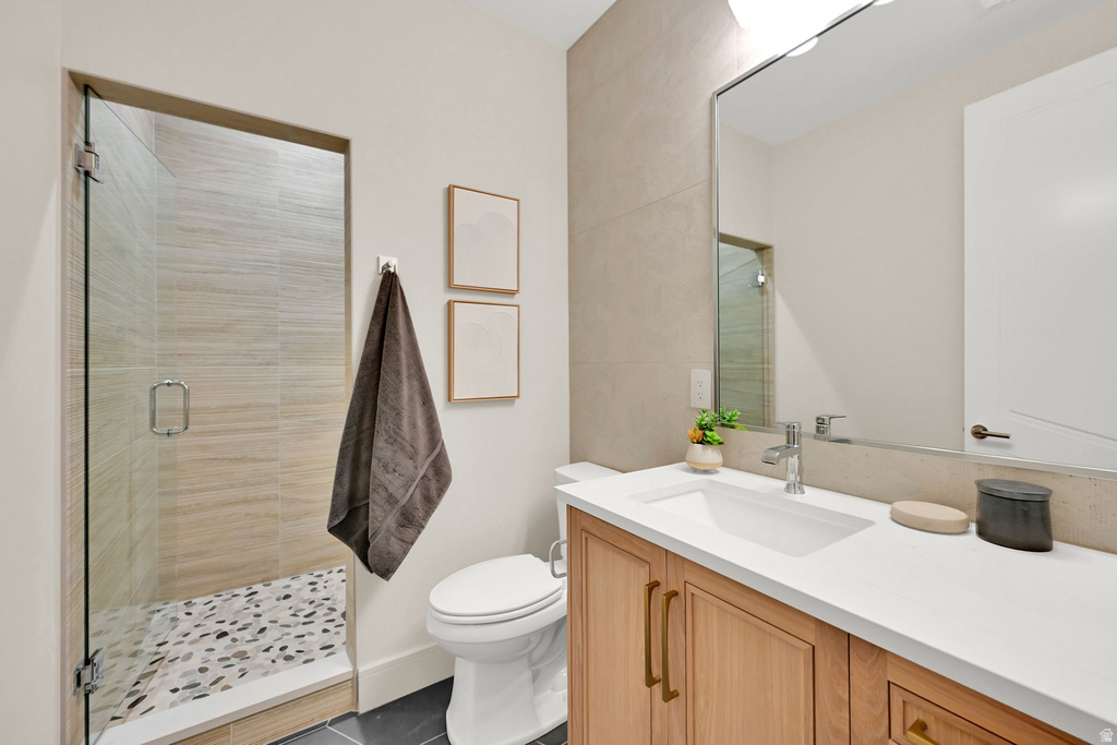 Bathroom featuring a glass-enclosed shower with pebble flooring and horizontal tile surround, a wood-finish vanity with a built-in sink, a large wall-mounted mirror, and a white toilet