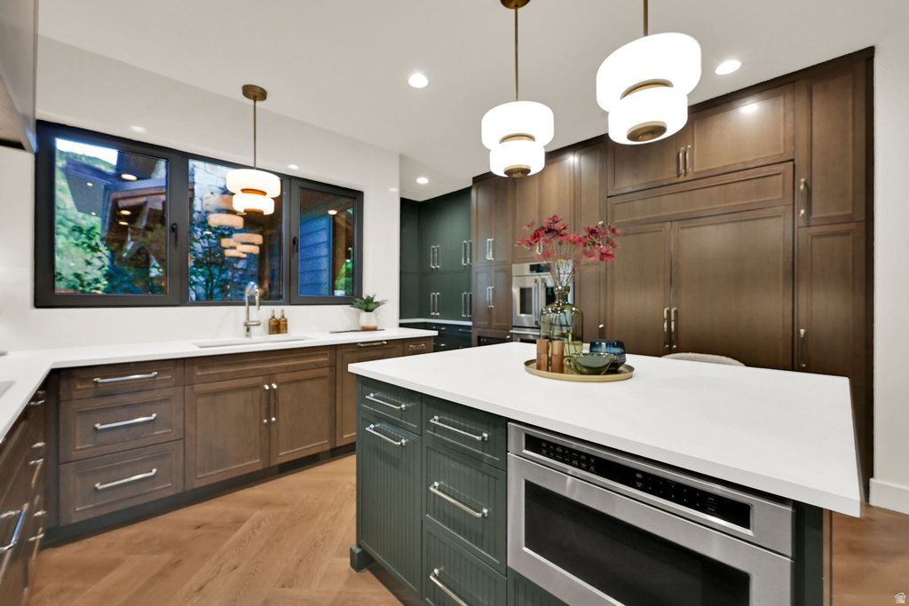 Modern kitchen featuring a large central island with an integrated microwave drawer, white countertops, and wood-finish flooring