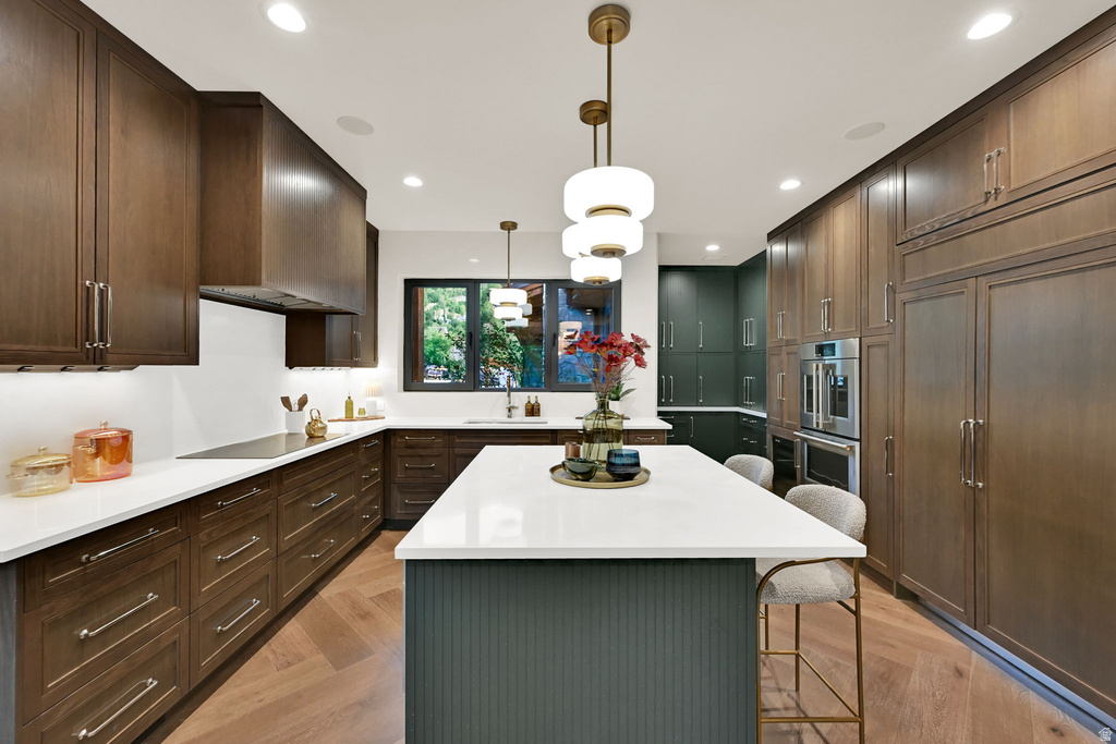 Modern kitchen featuring a central island with white countertop, extensive dark wood cabinetry, integrated stainless steel appliances, and herringbone wood-finish flooring