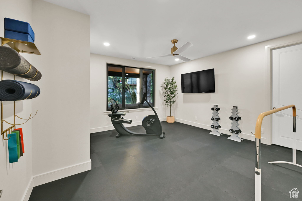 Dedicated exercise room featuring dark rubber flooring, a large window, a ceiling fan with integrated lighting, recessed lighting, and a wall-mounted display