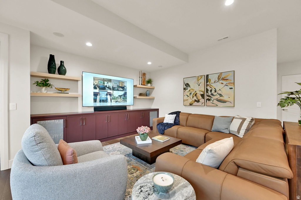 Recessed lighting illuminates a spacious living area featuring built-in cabinetry with a deep red finish, light wood floating shelves, and wood-finish flooring