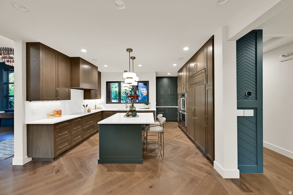 Kitchen featuring herringbone wood-finish flooring, a central island with a white countertop, dark wood-finish cabinetry, built-in stainless steel appliances, and recessed lighting