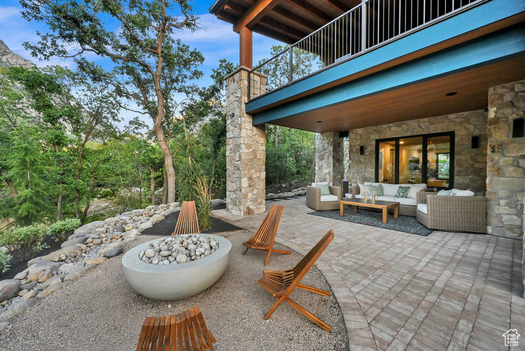 Expansive outdoor living area featuring a stone-clad exterior, covered patio with recessed lighting, and a contemporary fire pit