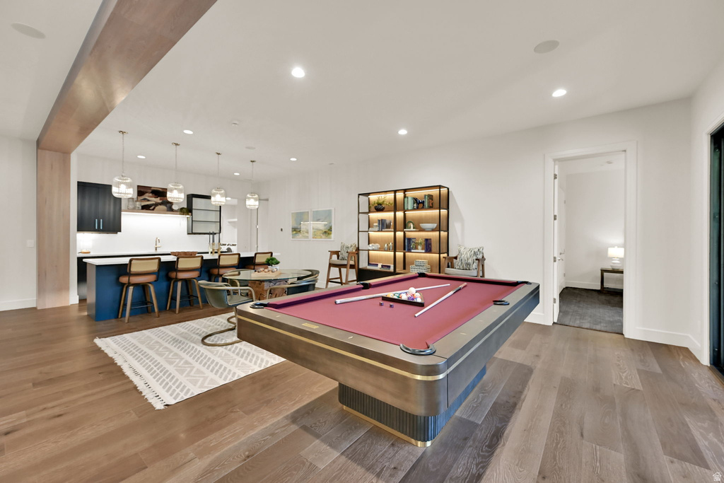 Open-concept recreation area featuring wood-finish flooring, a built-in wet bar with pendant lighting, and an illuminated display shelf