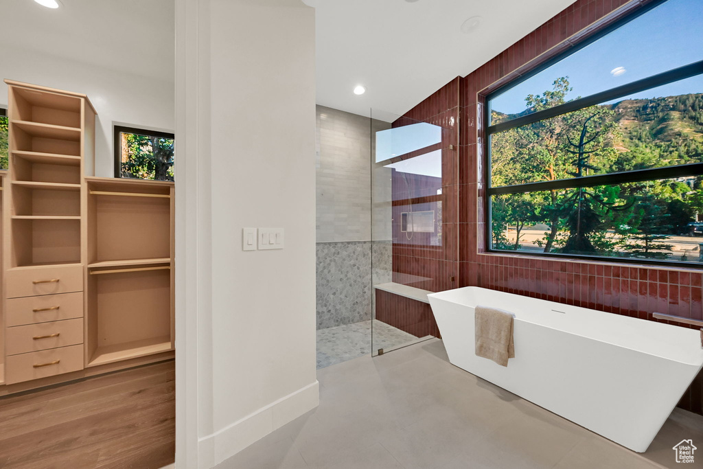 Freestanding soaking tub with a substantial window, large walk-in shower with a glass enclosure, and built-in closet system with drawers and shelving