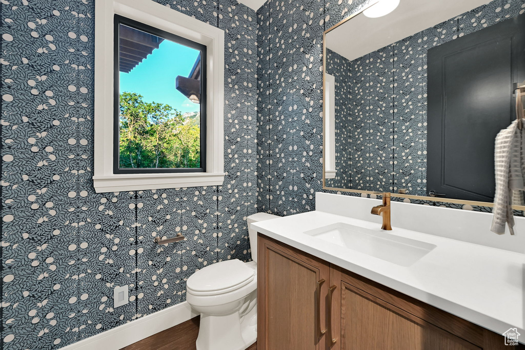Powder room featuring botanical-patterned wallpaper, a single window with white trim, and a wood-finish vanity with a white countertop and integrated sink