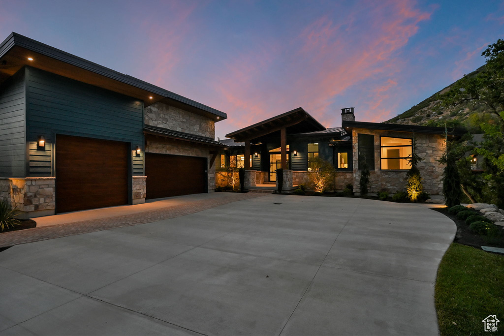 Stone and wood-finish siding exterior featuring multiple rooflines, a wide concrete driveway, and integrated outdoor lighting