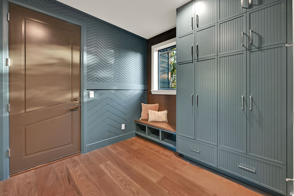 Entryway featuring a Dutch door, chevron-patterned accent wall, built-in window bench with storage, floor-to-ceiling cabinetry with beadboard detailing, and wood-finish flooring