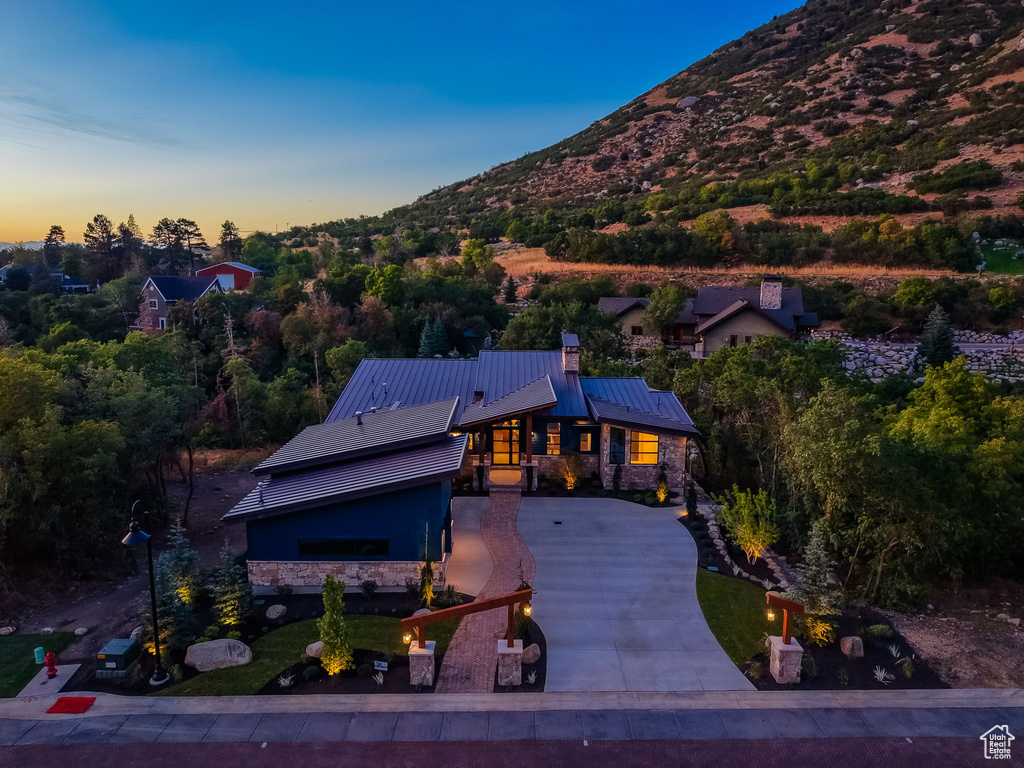 Contemporary residence featuring a stone and dark siding exterior, a metal roof, and a paved driveway with brick accents