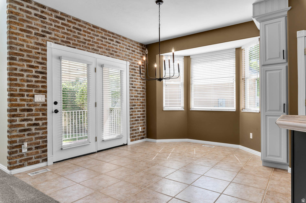 Tiled flooring throughout this dining area, featuring a brick accent wall, French doors with white trim, a bay window configuration with white blinds, and a built-in white cabinet with black hardware