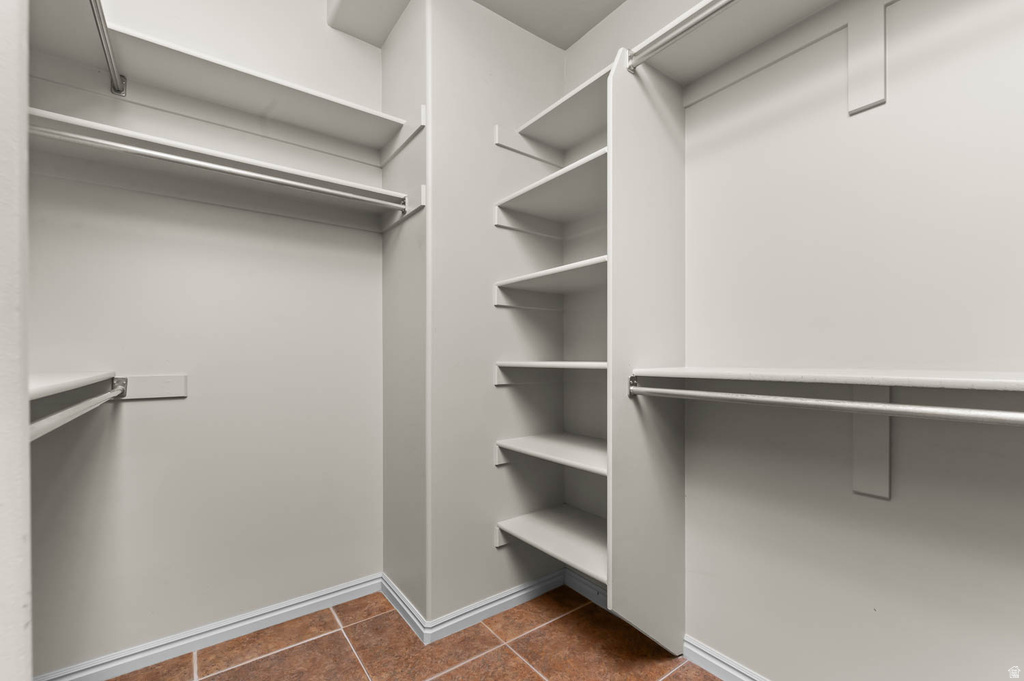 Spacious walk-in closet featuring multiple shelving units, double hanging rods, and terracotta-style tile flooring