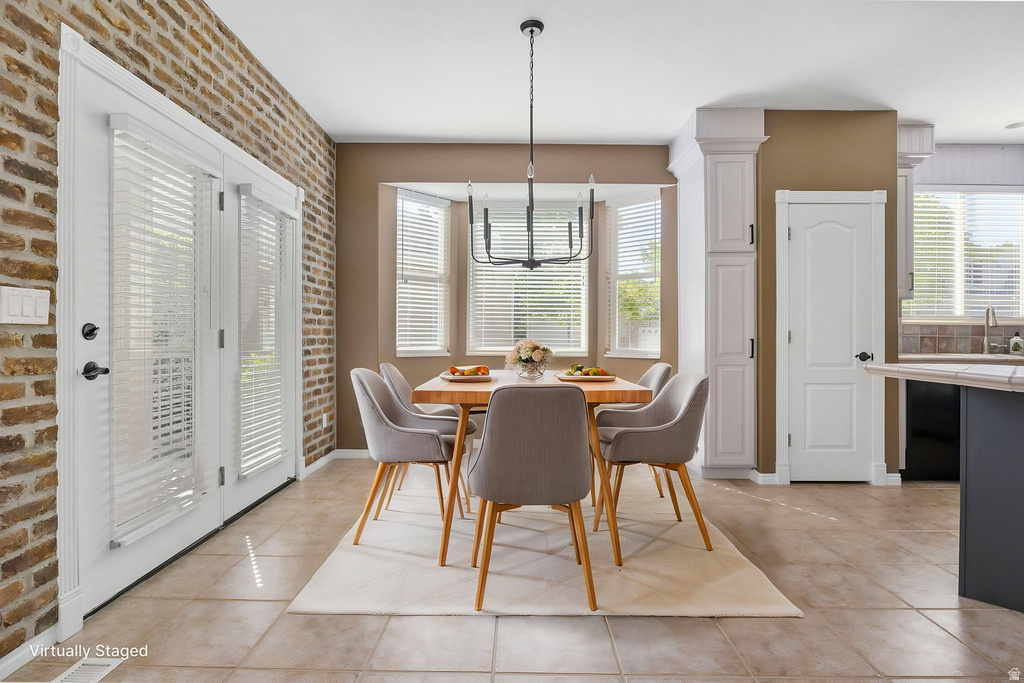 Dining area featuring a bay window, tile flooring, brick accent wall, and a modern chandelier