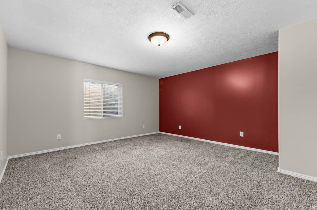 Spacious room featuring carpeting, a painted accent wall, and a window with blinds