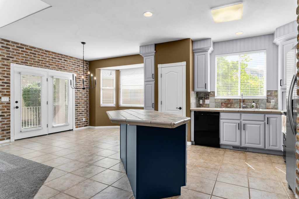 Kitchen featuring an island with a tiled countertop, light cabinetry, and black appliances