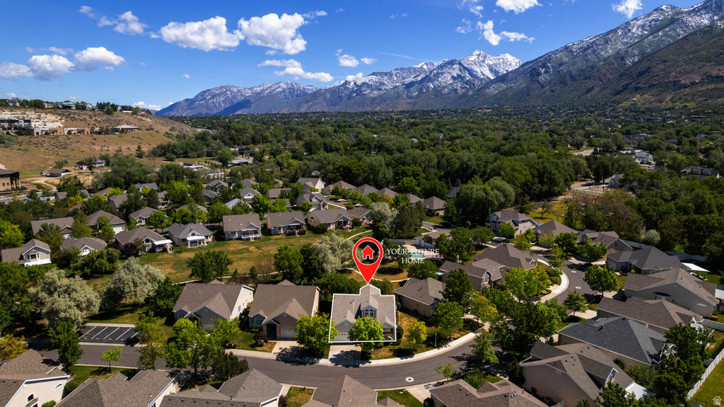 Aerial view showcasing a residential neighborhood with varied architectural styles and mature trees, set against a backdrop of snow-capped mountains and expansive green hills