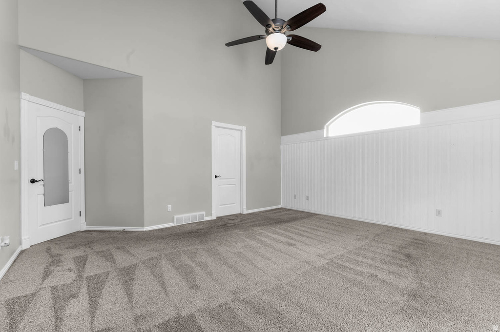 Vaulted ceiling room featuring light gray walls, a ceiling fan with integrated lighting, and a prominent arched window above white beadboard paneling