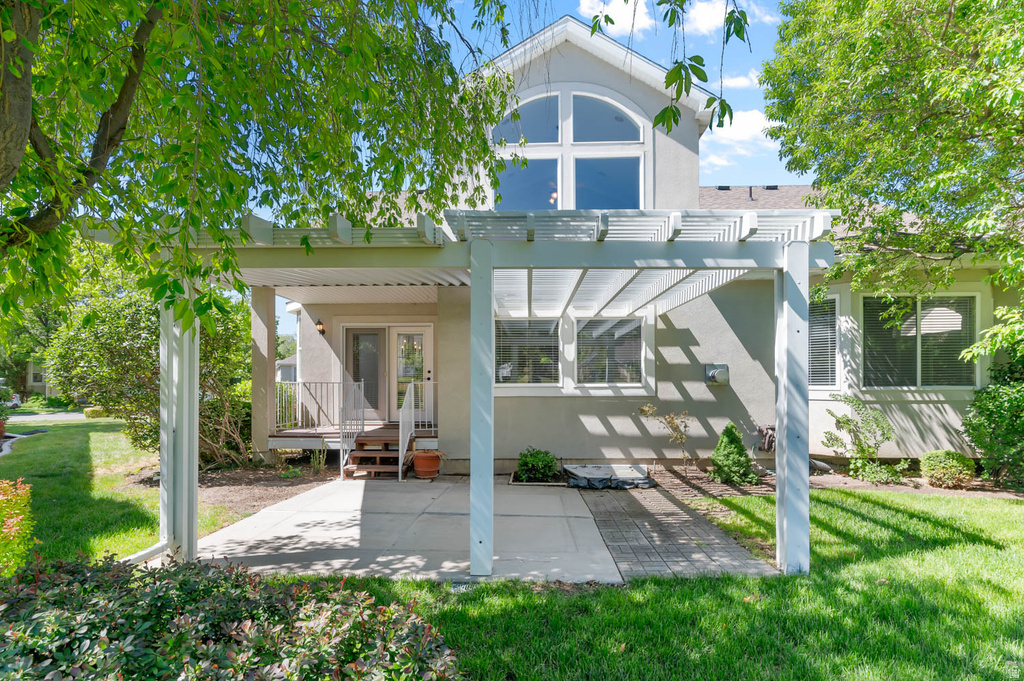 Rear exterior featuring a white pergola over a concrete patio and a second-story arched window