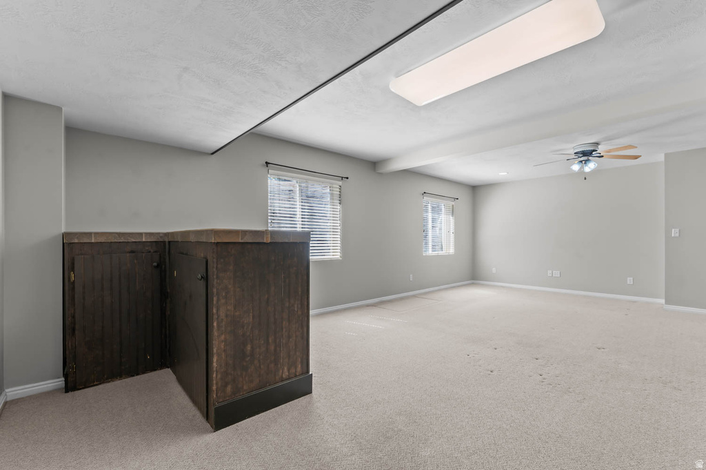 Spacious room featuring light-toned carpeting, two windows with blinds, and a built-in dark wood-finish cabinet with a tiled countertop