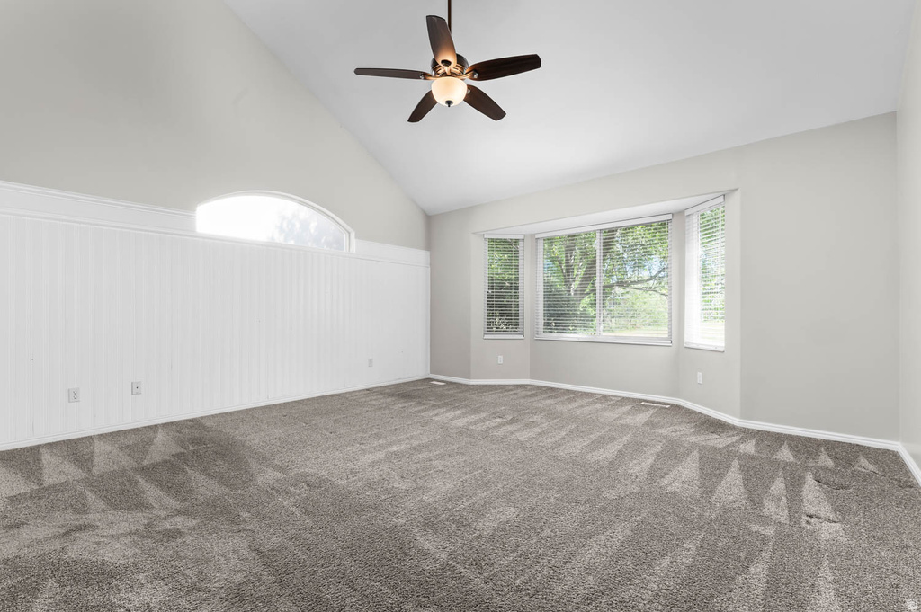 Spacious room with a vaulted ceiling, a multi-panel bay window, a semi-circular transom window, and white wainscoting